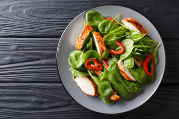Delicious salad of fresh baby spinach, chicken breast and bell pepper close-up on a wooden table. horizontal top view