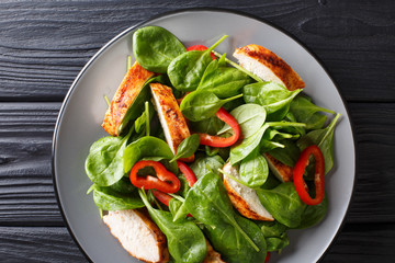 grilled chicken salad with fresh baby spinach and bell peppers closeup on a plate. Horizontal top view