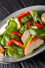 grilled chicken salad with fresh baby spinach and bell peppers closeup on a plate. vertical