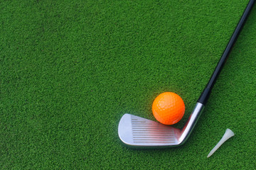 Golf equipment includes white and orange golf balls. Tee and golf clubs are placed on green grass in top view.