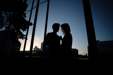 Silhouettes of couple (handsome man and young woman) in the city street with sky background