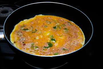 cooking omlette in Indian style with green chili , corriander leaves and lot of spices in a non stick pan