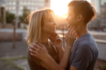 Couple of young handsome man and pretty woman look at each other in city street during sunset	