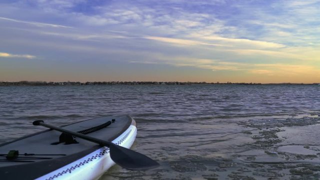 Stand up paddleboard on an icy lake shore after winter sunset - Boyd Lake State Park, Colorado