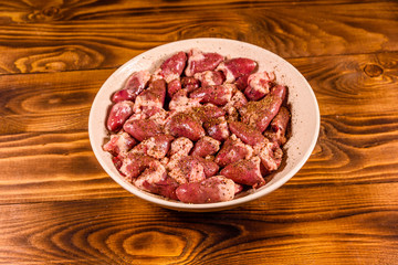 Ceramic plate with raw chicken hearts on wooden table