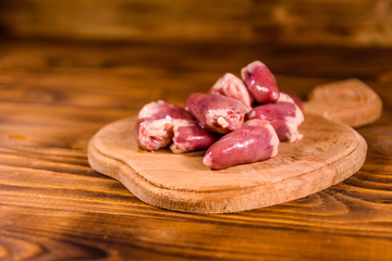 Cutting board with raw chicken hearts on wooden table