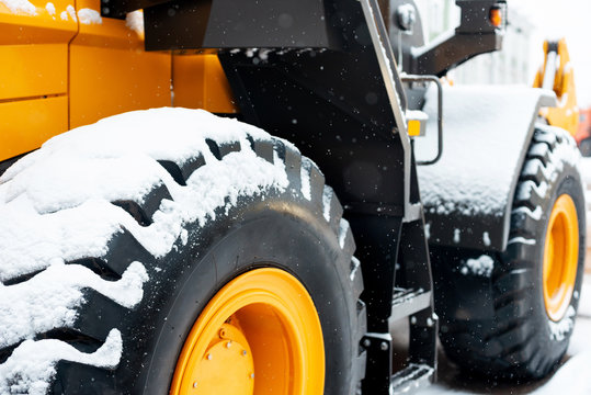 Snow covered tractor wheels. Yellow wheel front loader. Heavy diesel tractor, construction machinery, handling equipment, industrial vehicle. Winter time