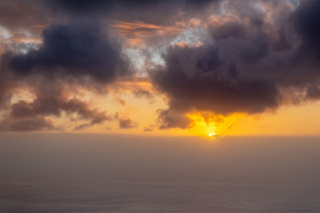 Beautiful sunset at the ocean with fog on the horizon and dark clouds in the sky