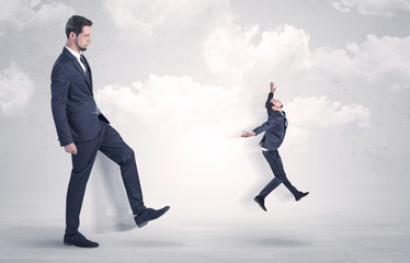 Big businessmen kicking himself as a small employee with cloudy background
