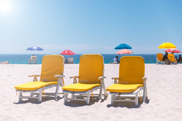 Three yellow beach chairs on a sunny day on Camps Bay sandy beach in Cape Town