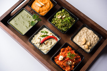 Group of Indian Chutneys includes coconut, Peanut, green and red chilly, garlic and pudina served in small square shape bowls. selective focus