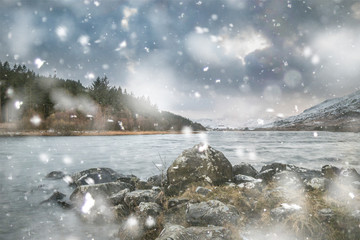 Beautiful Winter landscape image of Llynnau Mymbyr in Snowdonia National Park with snow capped mountains in background in heavy snow storm