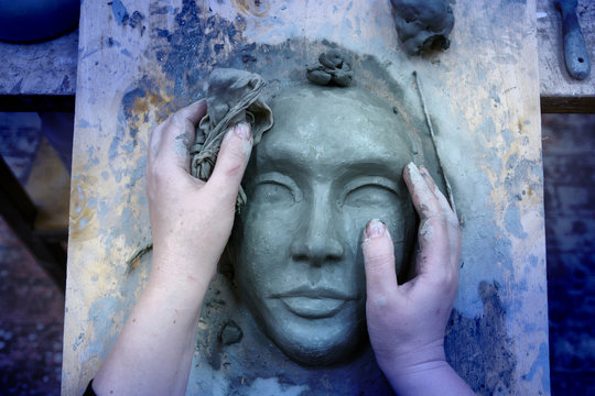 The hands of the sculptor mold the clay mask
