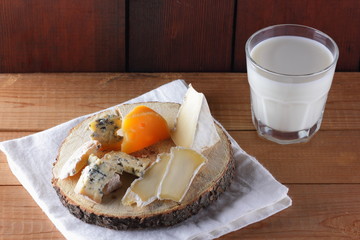 Various type of cheese and milk on wooden boards. Blue cheese, camembert and hard cheese on wooden stand. Dairy product on white napkin. Assortment of cheese and milk