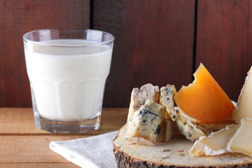 Various type of cheese and milk on wooden boards. Blue cheese, camembert and hard cheese on wooden stand. Dairy product on white napkin. Assortment of cheese and milk