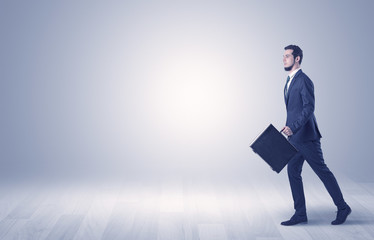 Fototapeta premium Successful businessman walking in front of an empty wall with briefcase on his hand 