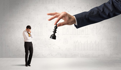 Little businessman is afraid to make the next step in his chess game with graphs, charts and...