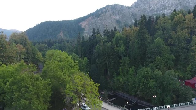 Aerial footage calm of a serene alpine mountain lake small village in mountains bridge over the river, people walk in the evening.