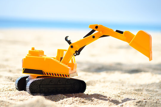bulldozer toy  ,dig machine toy  with sun light on the beach ,blue background.