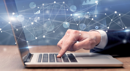 Businessman typing on laptop with linked reports charts grapghs around
