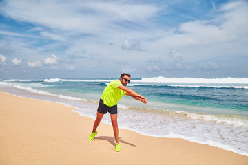 Sportsman stretching on a exotic tropical beach after jogging / exercising.