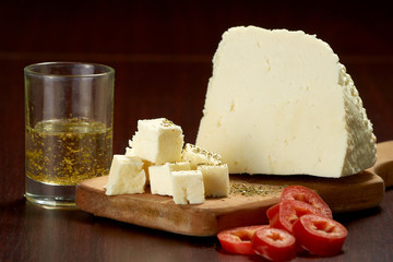 Slices of delicate white cheese and red sweet pepper on a wooden plank.