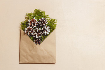 Top view green fir tree branches and cones in brown craft envelope on brown color wood background