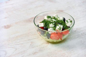 Transparent bowl with salad on a white wooden table