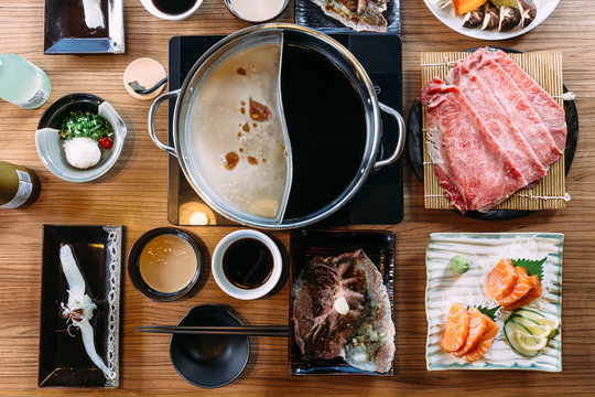 Top view of Shabu set including rare slices Wagyu A5 beef, Shabu shoyu and clear base, salmon, sushi and vegetables. 