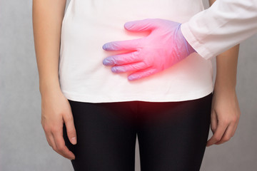 A doctor in medical gloves holds a girl by the lower abdomen which has problems with menstruation...