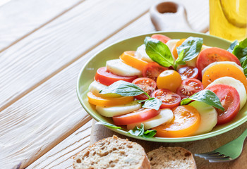 Close-up green plate with traditional Italian Caprese salad on kitchen board on wooden table.
