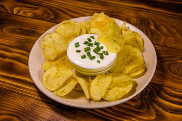 Ceramic plate with potato chips and glass bowl with sour cream on wooden table