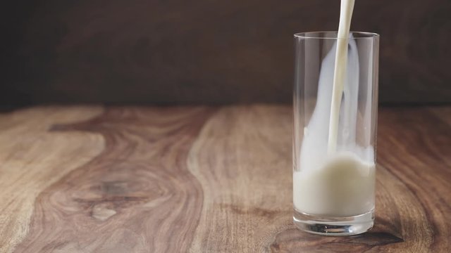 slow motion of pouring milk into the glass on wood table with copy space