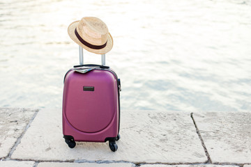 Pink suitcase with straw hat and map on sea coast. Concept of travel, vacation, tourism, adventure.