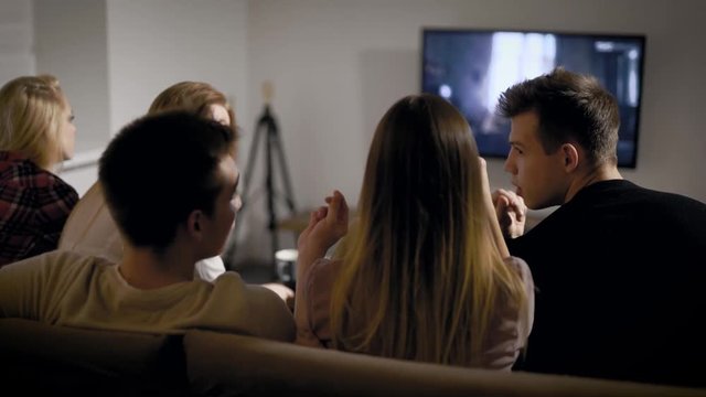 Group Of Friends Are Watching Scary Movie By Tv Monitor In Night Time In Home, Back View Of Their Heads