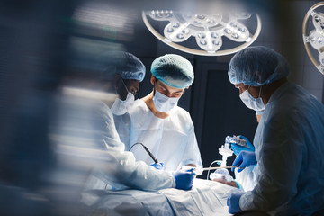 Blurred figures of surgeons in medical uniforms performing surgery in operation theatre, copyspace