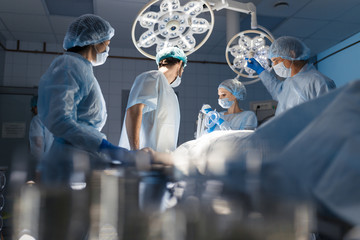 Blurred figures of surgeons in medical uniforms performing surgery in operation theatre, copyspace