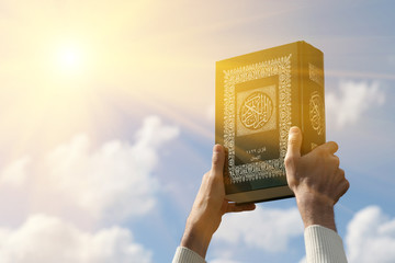 Man's hands holds Koran - holy book of muslims, on blue sky with clouds. With instagram style filter