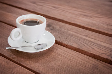 a cup of coffee on a saucer and a spoon stands on a wooden table. aromatic hot fresh coffee. wooden vintage table background with diagonal lines. for design and decor. selective focus