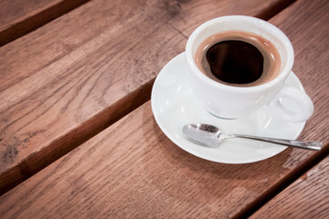 a cup of coffee on a saucer and a spoon stands on a wooden table. aromatic hot fresh coffee. wooden vintage table background with diagonal lines. for design and decor. selective focus