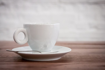 a cup of coffee on a saucer and a spoon stands on a wooden table. aromatic hot fresh coffee. wooden vintage table background with diagonal lines. for design and decor. selective focus