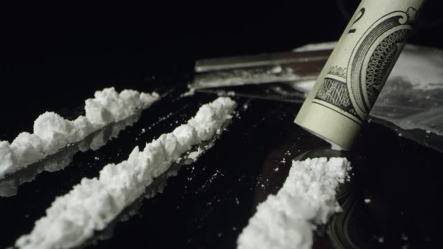 Up close view of white powdered drug being snorted while moving over lines of cocaine on black table top.