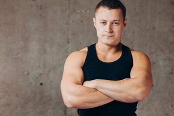 Obraz premium young confident strong sportsman standing with crossed arms at gym. close up photo. hobby, free time, lifestyle. copy space