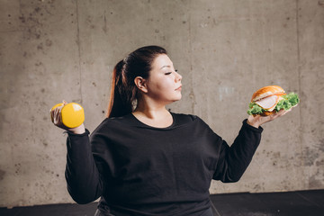 Obese man holding dumbbell eating burger, refusing from doing sport, addiction. close up photo