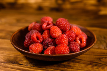 Ceramic plate with ripe raspberries on wooden table