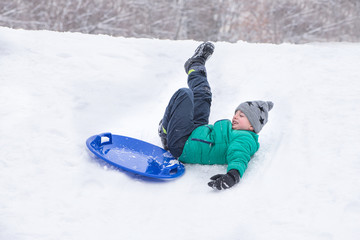Fototapeta na wymiar Boy falls rolling down a hill on snow saucer. Winter games