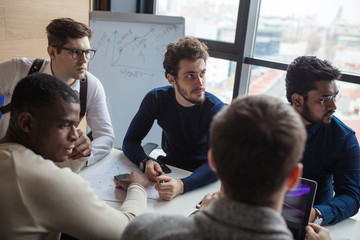 Multiethnic business team sitting at conference meeting table listening to speaker presenting innovation approaches for effective marketing strategies development and creative solutions.
