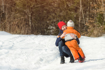 Mum embraces the small son on a background of pine forest. Winter snowy day in the coniferous forest