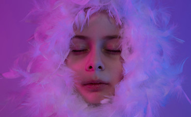 Child girl face surrounded by feathers with closed eyes