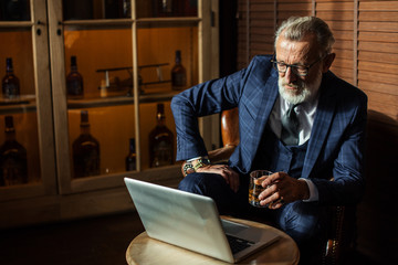 Confident and wealthy aged man in suit of clothes working from home on laptop computer sitting at...